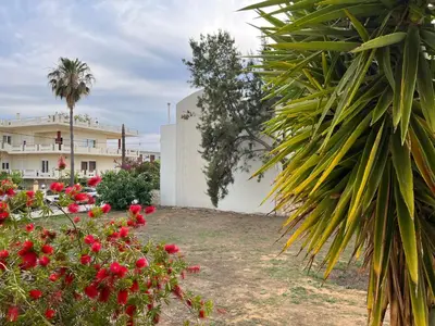 a garden with red flowers and a building at Seaside cozy apartment in Aghii Apostoli