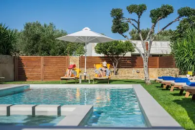 two people sitting in chairs by a pool with an umbrella at Villa Georgia Heated Pool & Jet-Tub in Kolymvari