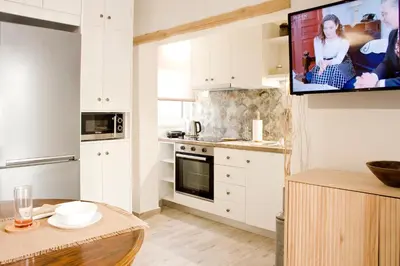 a kitchen with white cabinets and a tv on the wall at Sia's Sea House in Almirida