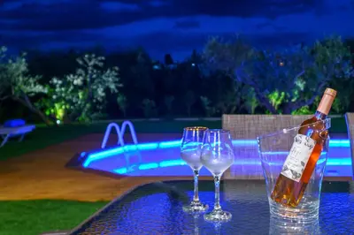 three wine glasses and a bottle on a table near a pool at Villa Lima Pool & Jacuzzi Chania in Vamos