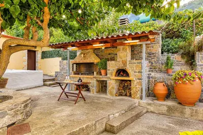 a patio with a stone oven with a table and a tree at Pomogna house in Pemónia