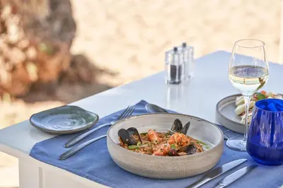 a table with a bowl of food and a glass of wine at Atlantica Kalliston Resort - Adults Only in Stalos