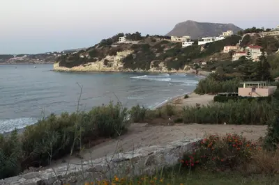 a beach with houses on a hill next to the ocean at kera apartments in Kalyves