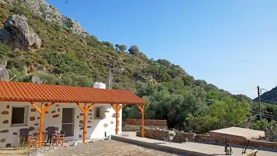 a building with a table and chairs in front of a mountain at Polyraki's Cottage in Chania Town