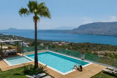 a woman sitting next to a swimming pool with a palm tree at Villa Damant in Pithárion