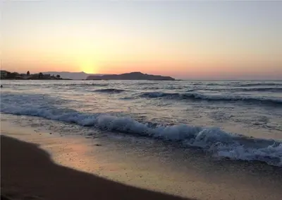 a beach with the sun setting in the ocean at glarosmaisonette in Kato Daratso