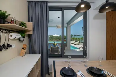 a kitchen with a table and a view of a pool at Cretan Queen Residences in Aghii Apostoli