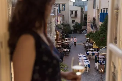 a woman looking out a window at a street with tables and chairs at Harismari Cozy Hotel in Chania Town