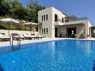 a swimming pool with chairs and umbrellas next to a house at Villa Karissa in Gavalochori