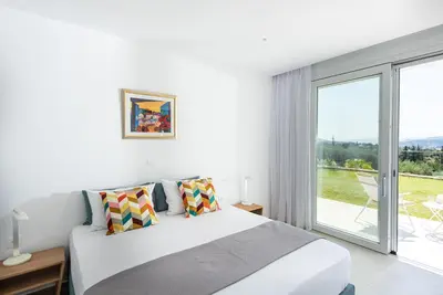 a white bedroom with a bed and a large window at Villa Inati in Nípos