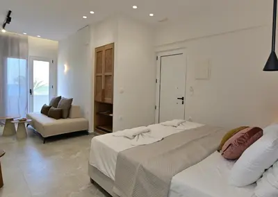 a white bedroom with a large bed and a chair at Morpheas Rooms in Palaiochóra