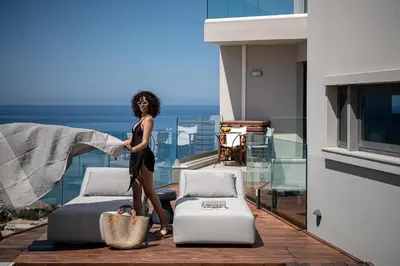 a woman in a black dress standing next to beds on a balcony at Alectrona Living Crete, Villa Ãcro in Plataniás