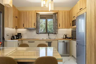 a kitchen with wooden cabinets and a table with chairs at Chris and Stratos villa with private ecologic pool and kid's playground! in Mourniaí