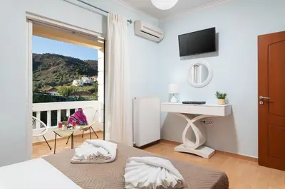 a bedroom with a bed and a desk and a balcony at Villa Ithaca in Varípetron