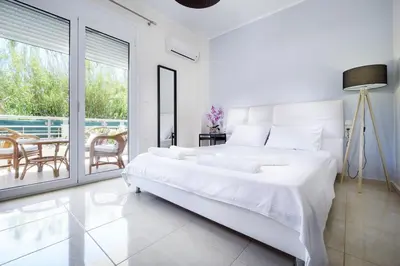 a white bedroom with a bed and a balcony at Geas House Ammos in Kolymvari
