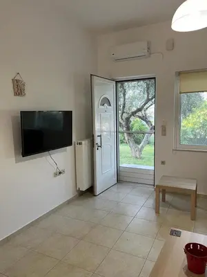 a living room with a door and a tv on the wall at AVRA COZY APARTMENT Agioi Apostoloi Chania in Daratso