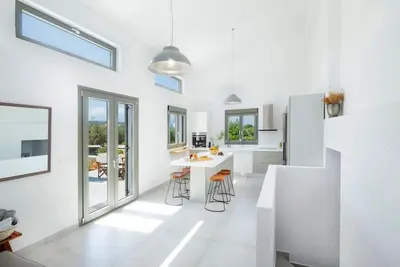 a white kitchen with a counter and stools at Olisea Villa, olive grove seaview villa in Kounoupidhianá
