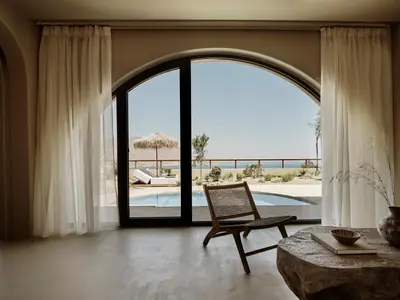 a living room with a chair and a large window at Tella Thera, a Member of Design Hotels in Kissamos