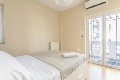 a white bedroom with a bed and a large window at Cozy Apartment 50m to beach, 5min walk to Old Town in Chania Town