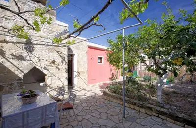 a patio with a table and a pink building at Levendi's House in Kissamos