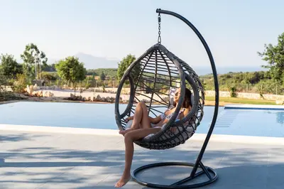 a woman sitting in a swing by a pool at Villa Annie Crete - Private Luxury Villa with Sea and Mountain Views in Tsivarás