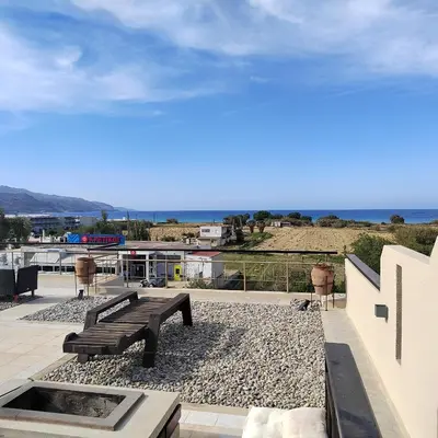 a bench on a patio with the ocean in the background at Rododafni Apartments in Kolymvari