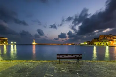a bench sitting next to a body of water at night at The Blue Studio, 1 min walk from Kalamaki beach in Kalamaki Chanion