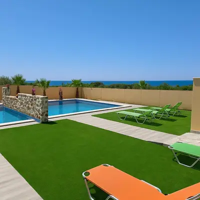 a swimming pool with green grass next to a resort at Paliochora Beachfront Escape, Milolithos Pool Retreats in Palaiochóra
