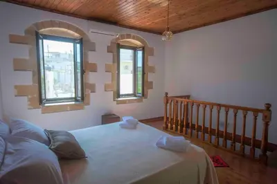 a bedroom with a large bed with two windows at Skaros Cottage in Chania Town