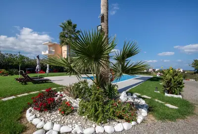 a garden with flowers and a palm tree next to a pool at Socrates Holidays Apt. 2 with Pool near the Beach in Plataniás