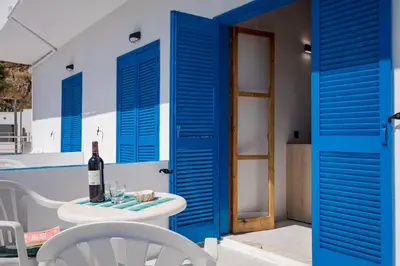 a room with blue shutters and a table with a bottle of wine at Finikas Resort Sfakia - Seaside Rooms in Loutro
