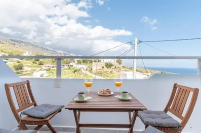 a table with two glasses of wine and two chairs at Avra Sfakia Apartments in Khóra Sfakíon