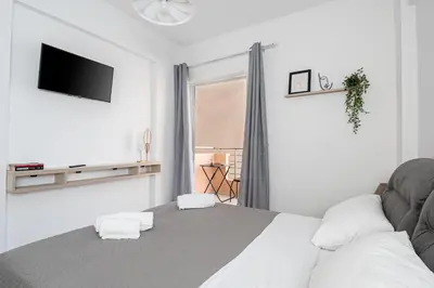 a white bedroom with a bed and a television at Niman Beachside Apartments in Chania Town