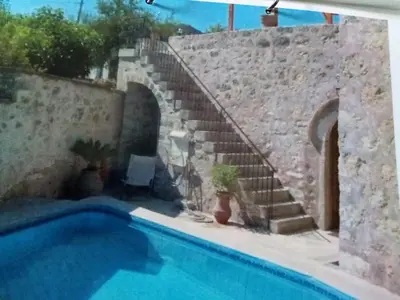 a swimming pool next to a stone wall with a staircase at Charmante maison crétoise à Embrosneros in Embrósneros