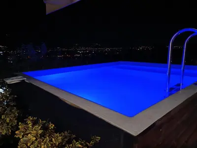 a swimming pool at night with a city skyline in the background at Thearia villa II private heated hydromassage pool in Souda