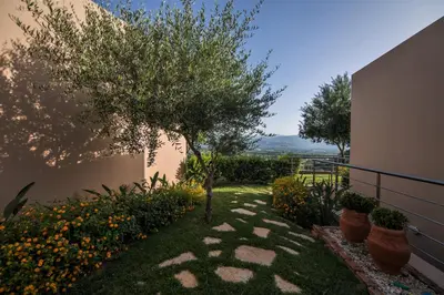 a garden with a tree and some plants and a building at Aksos Suites Accessible Accommodation in Ayiá