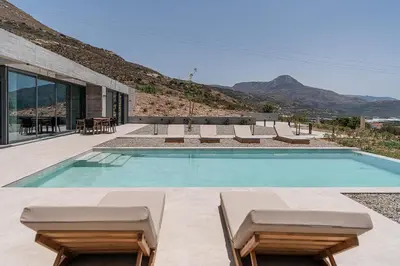 a swimming pool with chairs and a house at Alba Cave Villas in Chania Town