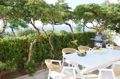a white table and chairs on a patio with trees at NAOS-Sea front vacation rental by Chania center in Chania Town