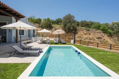 a pool with chairs and umbrellas next to a house at Villa Wisdom - Elegant & Homely with Pool, Galatas in Chania Town