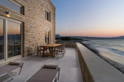 a patio with a table and chairs next to the water at Villa Maistros in Kissamos