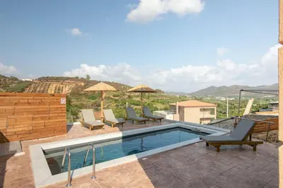 a swimming pool with chairs and umbrellas on a building at Villa Elpida in Myloniana in Milonianá