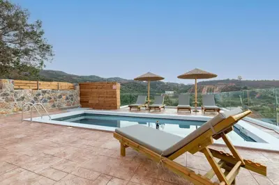 a swimming pool with chairs and umbrellas on a patio at Villa Elpida in Myloniana in Milonianá