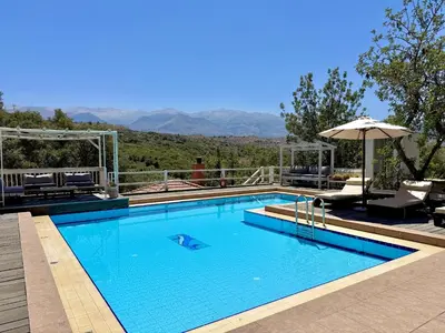 a swimming pool with an umbrella and a view of mountains at Villa Amvrosia Nr Kalives Crete in Arménoi