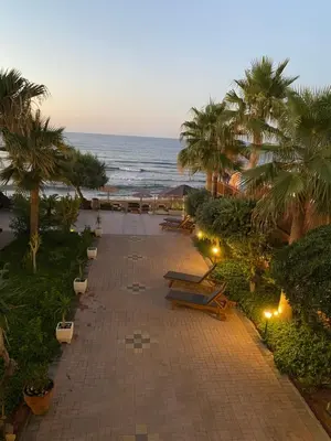 a walkway with benches and palm trees and the ocean at Be Crete - Zen Appartments 1 room in Agia Marina Nea Kydonias