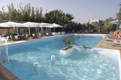 a large swimming pool in a resort with tables and umbrellas at Proimos Apartments in Gerani Chanion