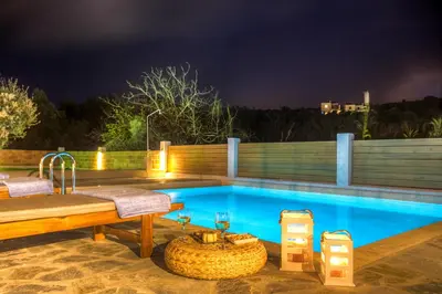 a swimming pool at night with a bench and a table at Cyan Icons Villas Kalyves Chania in Kalyves