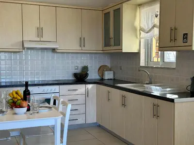a kitchen with white cabinets and a white table at Aegean View Villa, 2-min Drive to Almyrida Beach in Almirida