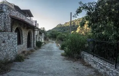 a dirt road next to a stone building with a fence at Diving into silence - Traditional Stone House in Kakópetros