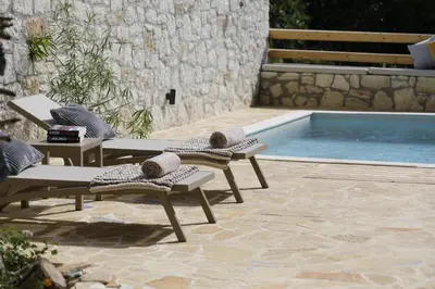 a pool with two chaise lounges next to a pool at Tholos by Praxithea Stone House & Pool in Gavalochori