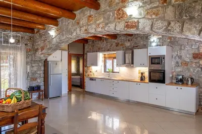 a kitchen with white cabinets and a stone wall at Villa Kamaraki in Patellárion